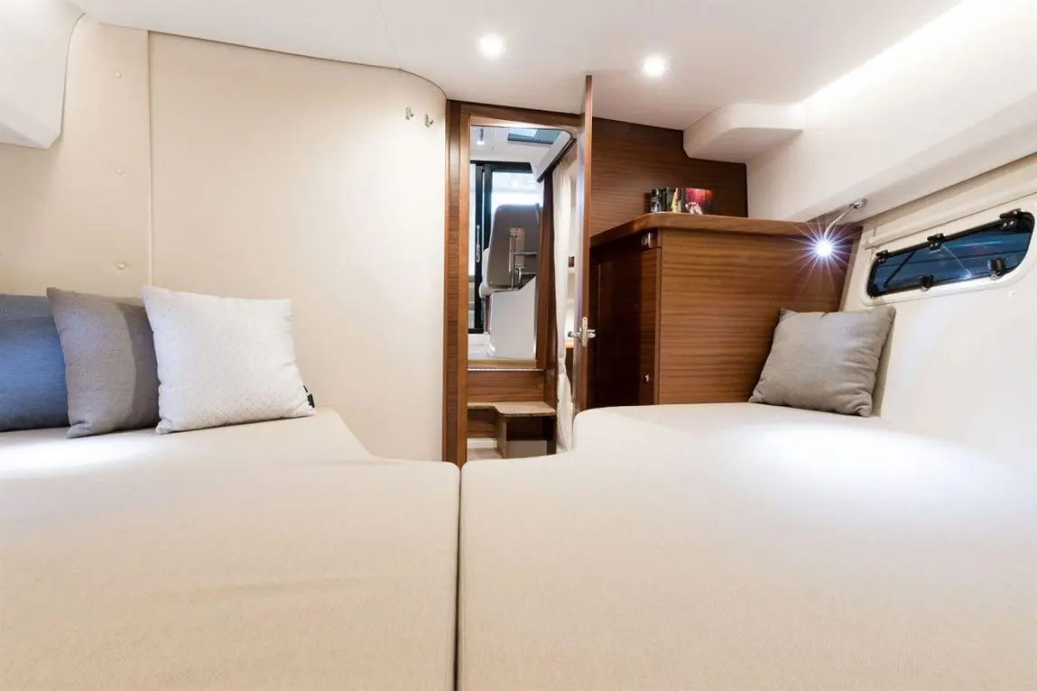 Interior of a modern yacht cabin with two beds, soft cushions, wooden storage unit, and a staircase leading to another area.